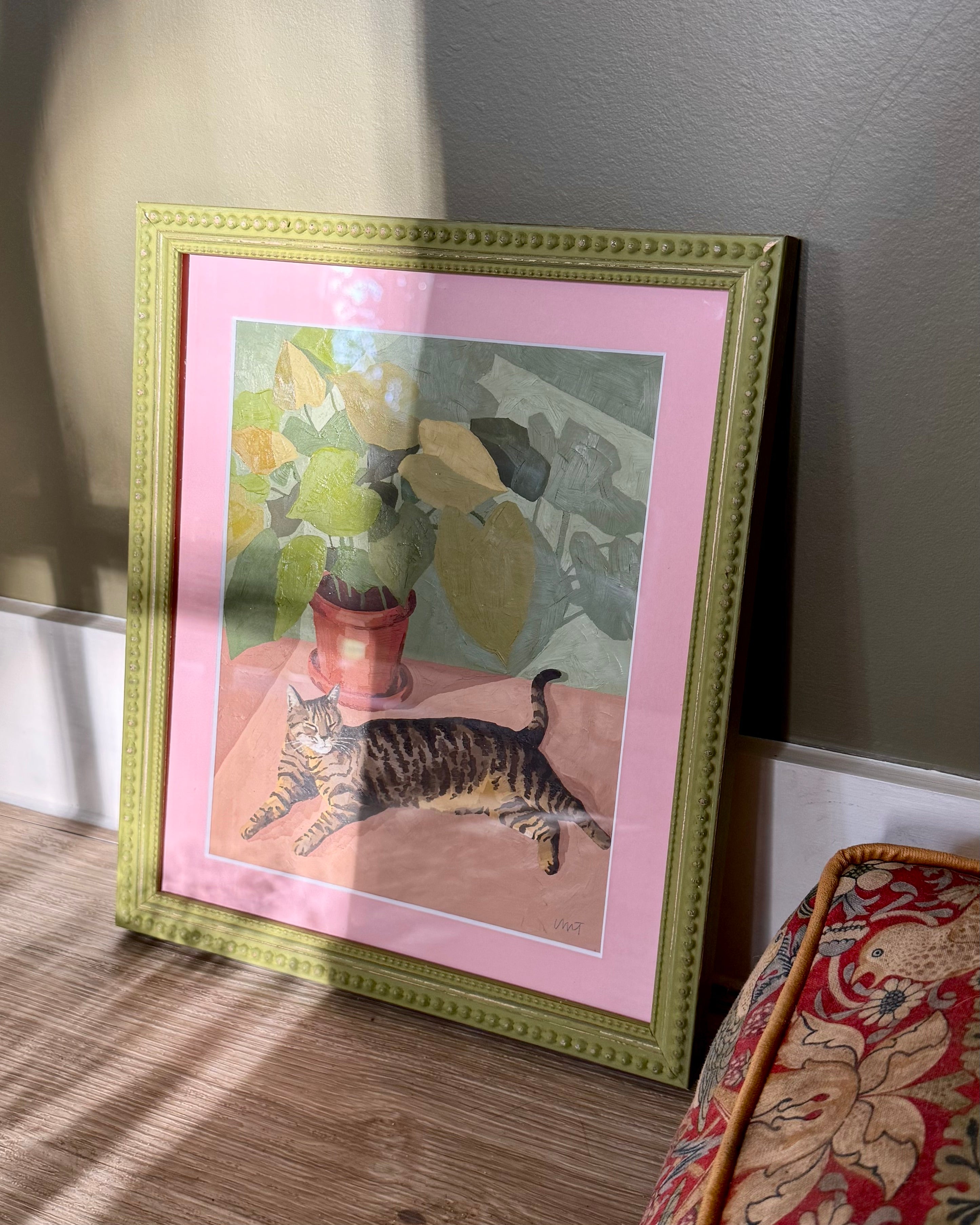 Framed artwork of a cat on a pink background with a green frame.