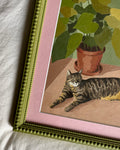 Framed artwork of a cat sitting next to a potted plant on a textured surface.