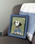Framed picture of a dalmatian dog on a gray armchair with a blue blanket.