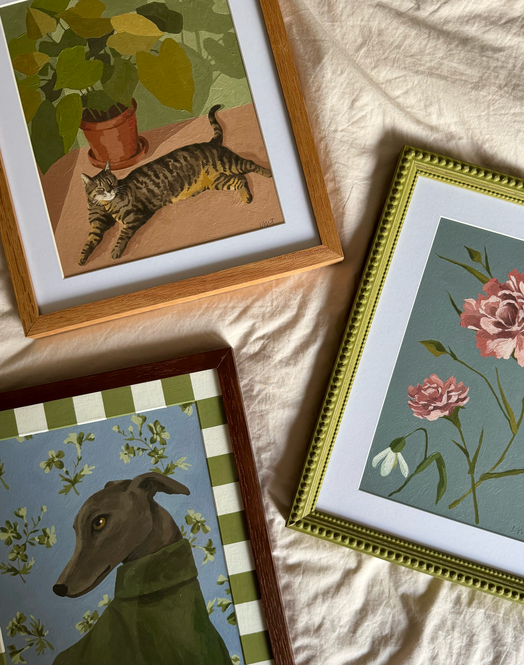 Framed artworks of a cat, dog, and flowers on a textured surface