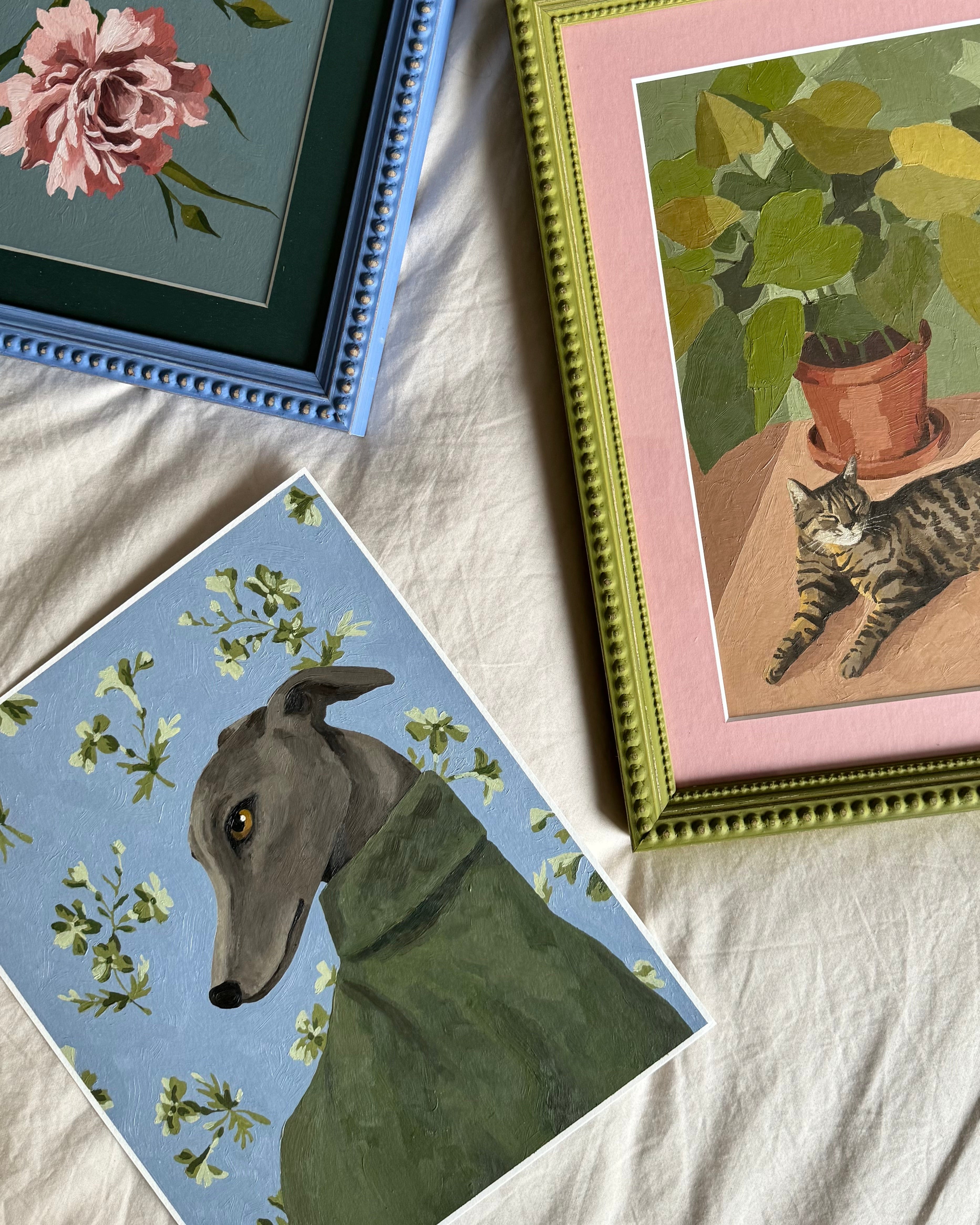 Three framed artworks on a textured surface, featuring a dog, a cat, and floral elements.